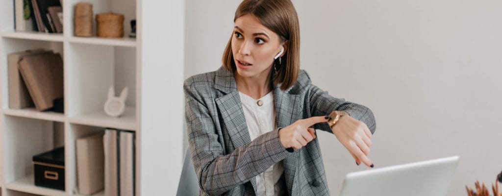 Lady boss in stylish outfit points out to clock, talking about late of her subordinate. Portrait of woman sitting in light office